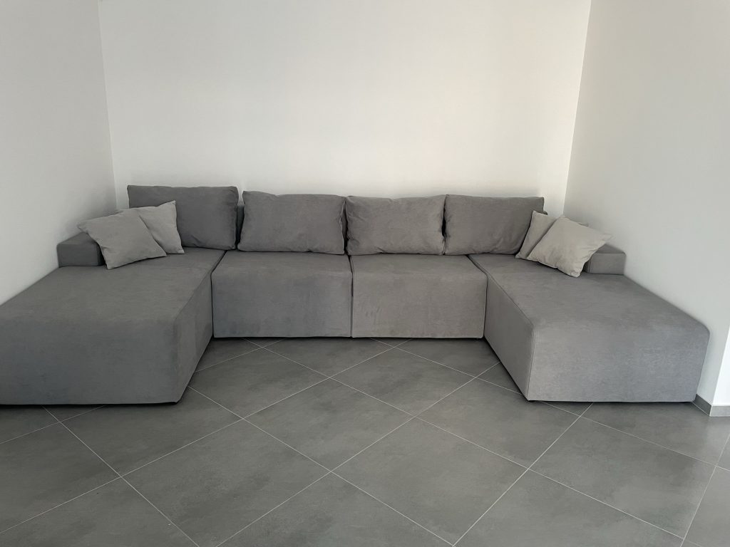 jasnoszara sofa w ksztalcie u w malym mieszkaniu dla studentki